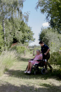 Carer from Choice Care 4U providing respite care services, pushing an elderly client in a wheelchair through a peaceful backyard garden.