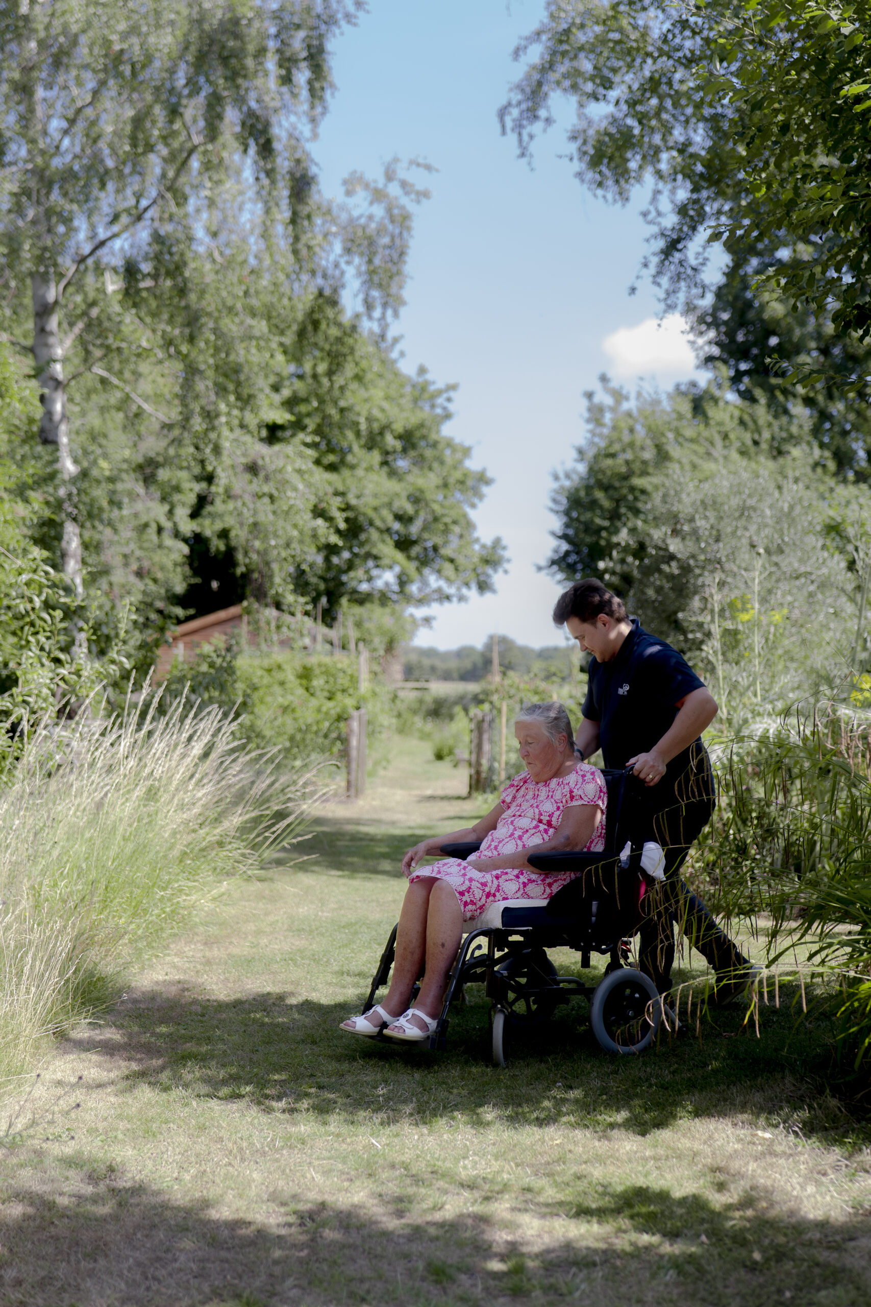 Carer from Choice Care 4U providing respite care services, pushing an elderly client in a wheelchair through a peaceful backyard garden.