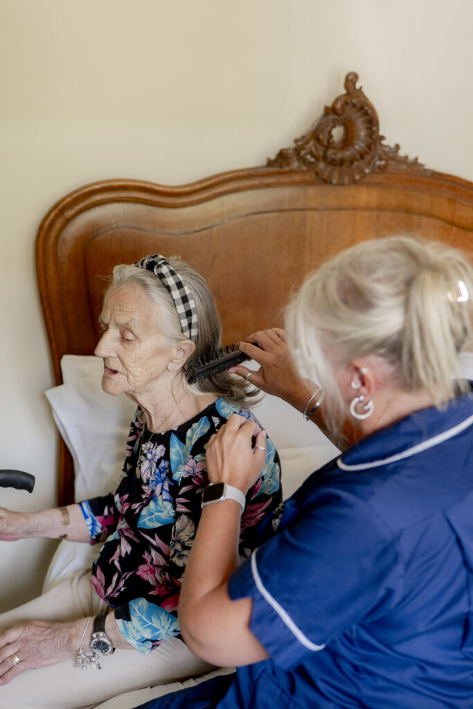 Carer from Choice Care 4U providing dementia home care services, gently combing an elderly woman's hair while sitting beside her bed in a calm and caring environment.