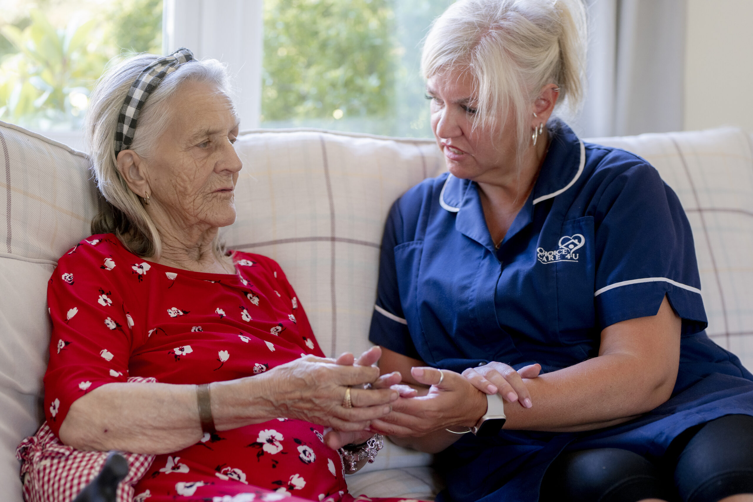 A Choice Care 4U carer providing companionship care, sitting on a couch and warmly chatting with an older woman in a comfortable home setting.
