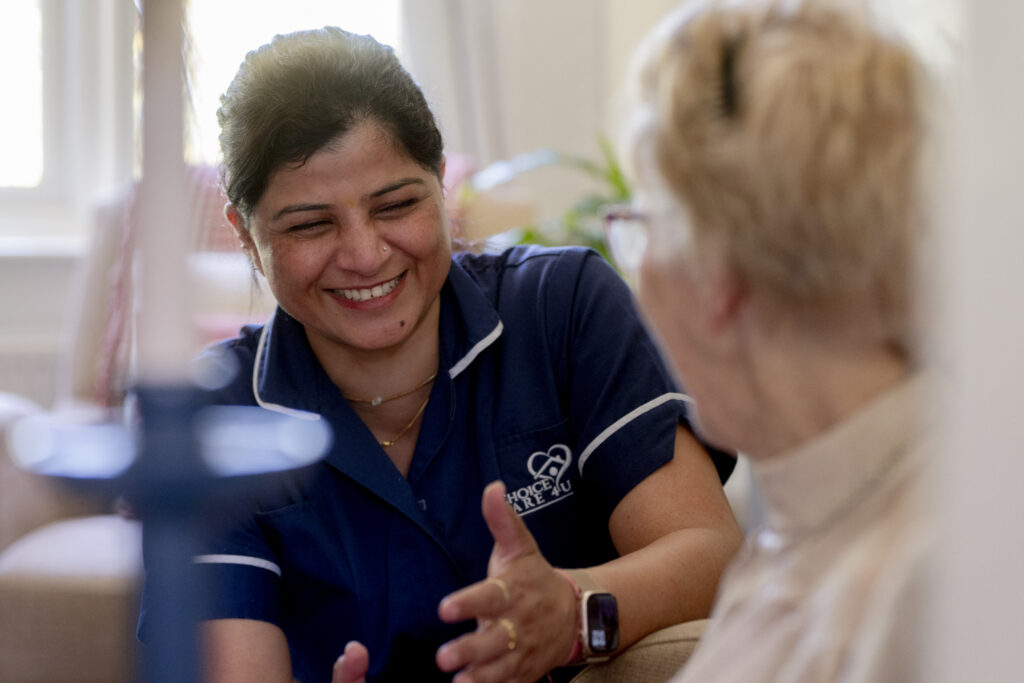 Carer from Choice Care 4U smiling warmly at an elderly client during a home visit, representing compassionate palliative home care services in West Sussex.
