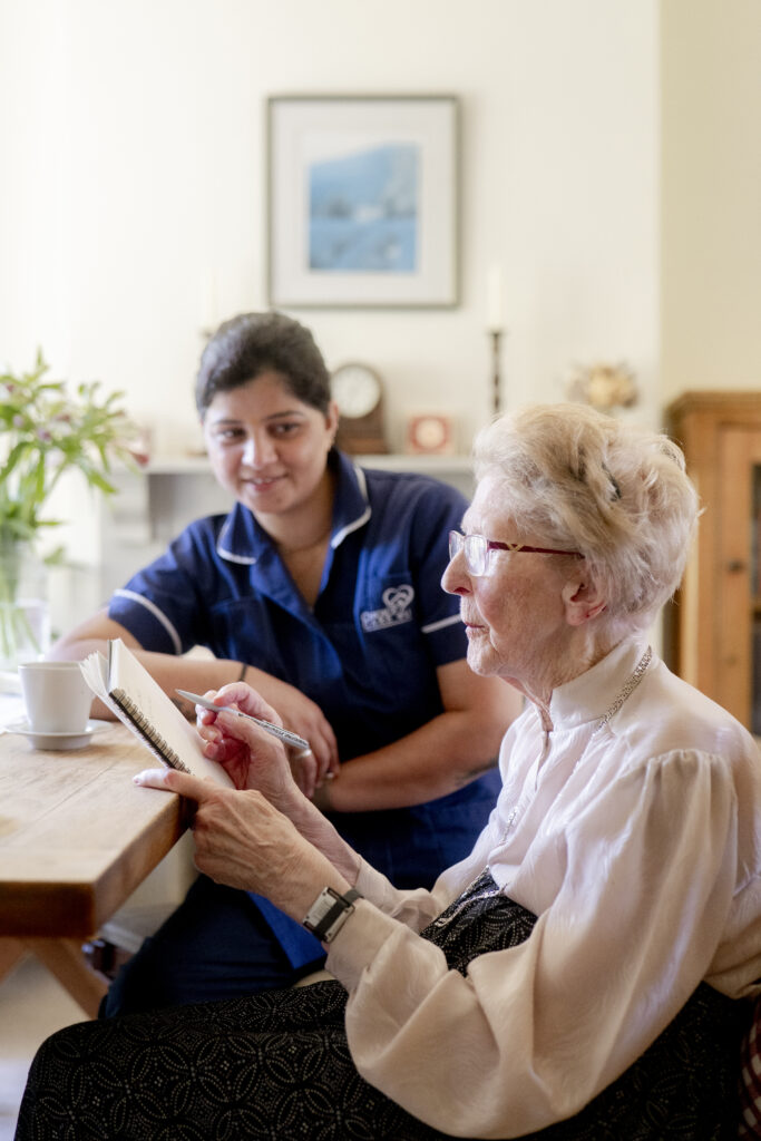Carer from Choice Care 4U providing compassionate support to an elderly client while taking notes, representing professional dementia home care services in West Sussex.