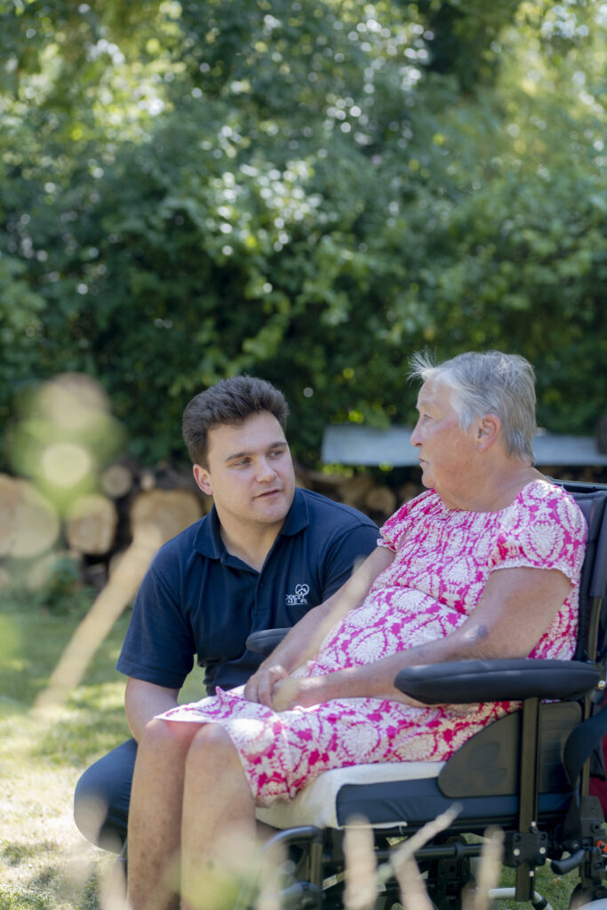 Carer from Choice Care 4U sitting at eye level with an elderly client in a wheelchair, engaging in a warm conversation, demonstrating compassionate palliative home care services in a comfortable home setting.