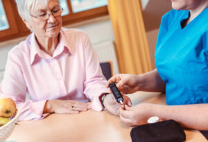 A diabetic woman receiving a finger prick blood test from a caregiver at home, demonstrating compassionate diabetes home care support.