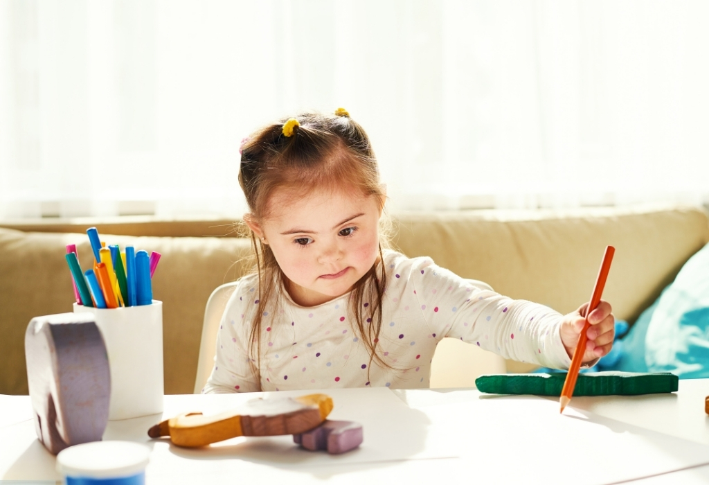 Disabled child sitting alone at a table, holding a pencil, highlighting the importance of specialist home care support.