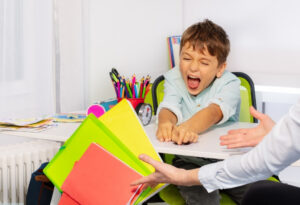 Young autistic child experiencing frustration during a learning activity at home, with a carer offering support and understanding through respite care for autism services in a calm and structured environment.