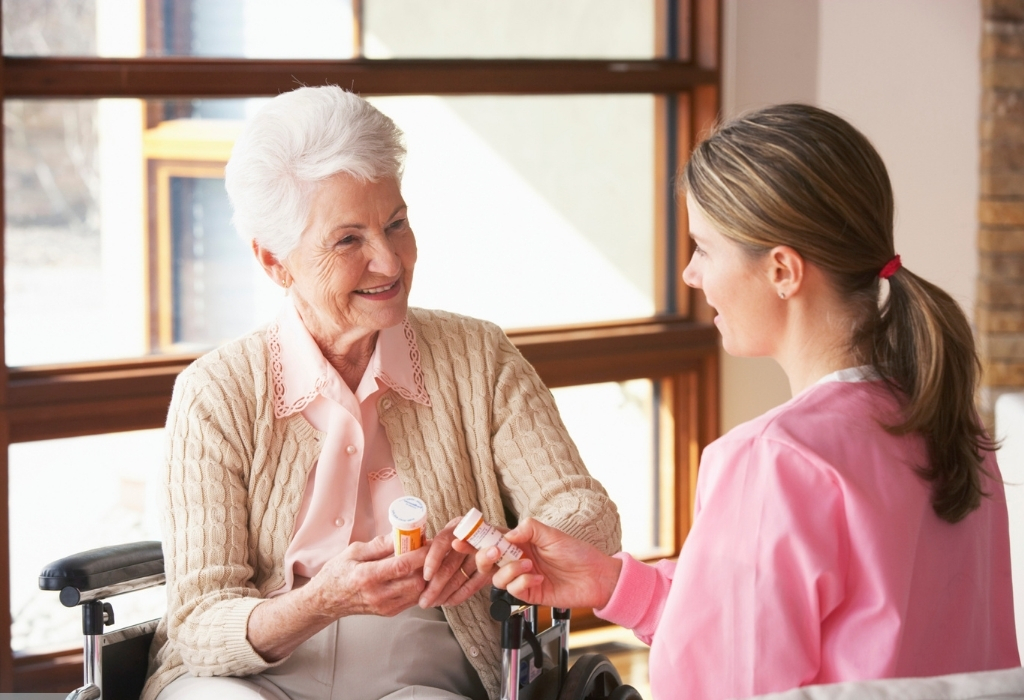 An elderly woman and her carer face each other while holding an insulin pen at home, representing compassionate Diabetes Home Care support and assistance.