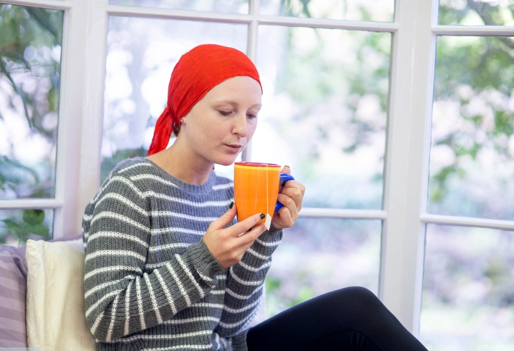 Care at Home for Cancer Patients – woman with cancer drinking tea in a peaceful home environment, receiving comfort and support.