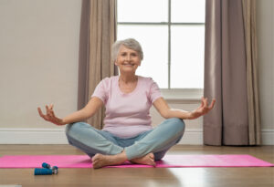 Senior woman performing yoga with carer at home in West Sussex.
